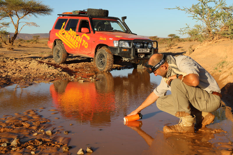 Load image into Gallery viewer, Person crouching by a puddle with a red off-road vehicle in the background
