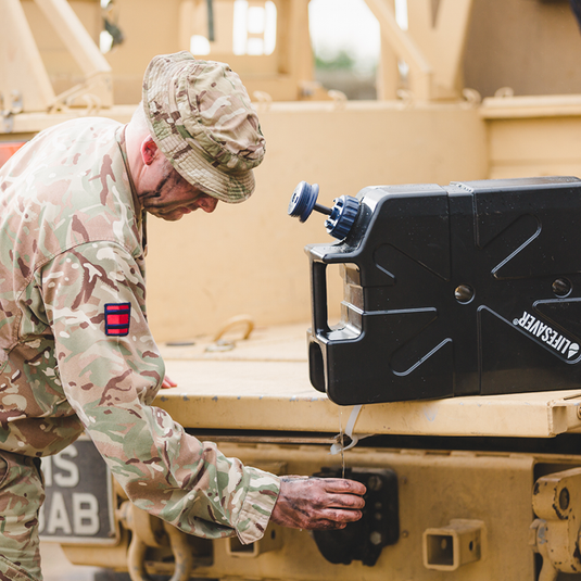 Soldier in camouflage uniform filling a cup from a black LifeSaver Jerrycan on a military vehicle