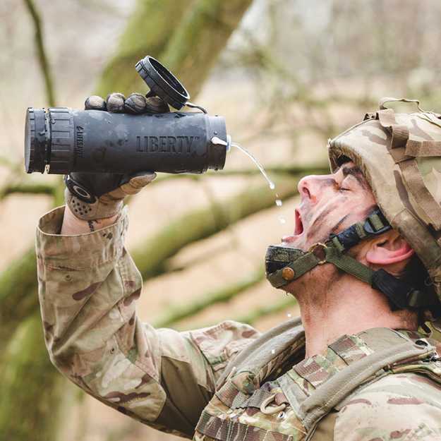 Load image into Gallery viewer, Person in military gear drinking from a Liberty water bottle outdoors.
